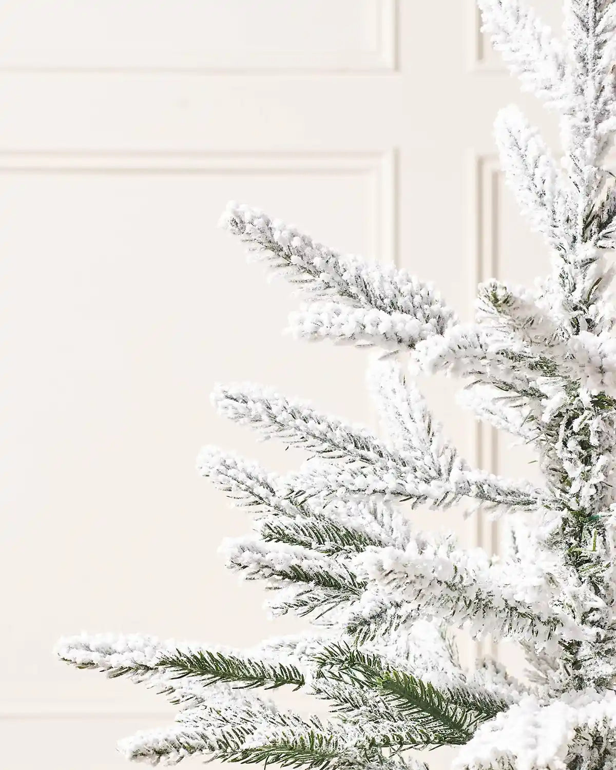 Close up of 2ft Snow flocked artificial Christmas tree tips with a brown hessian-wrapped base on a cream panel textured background
