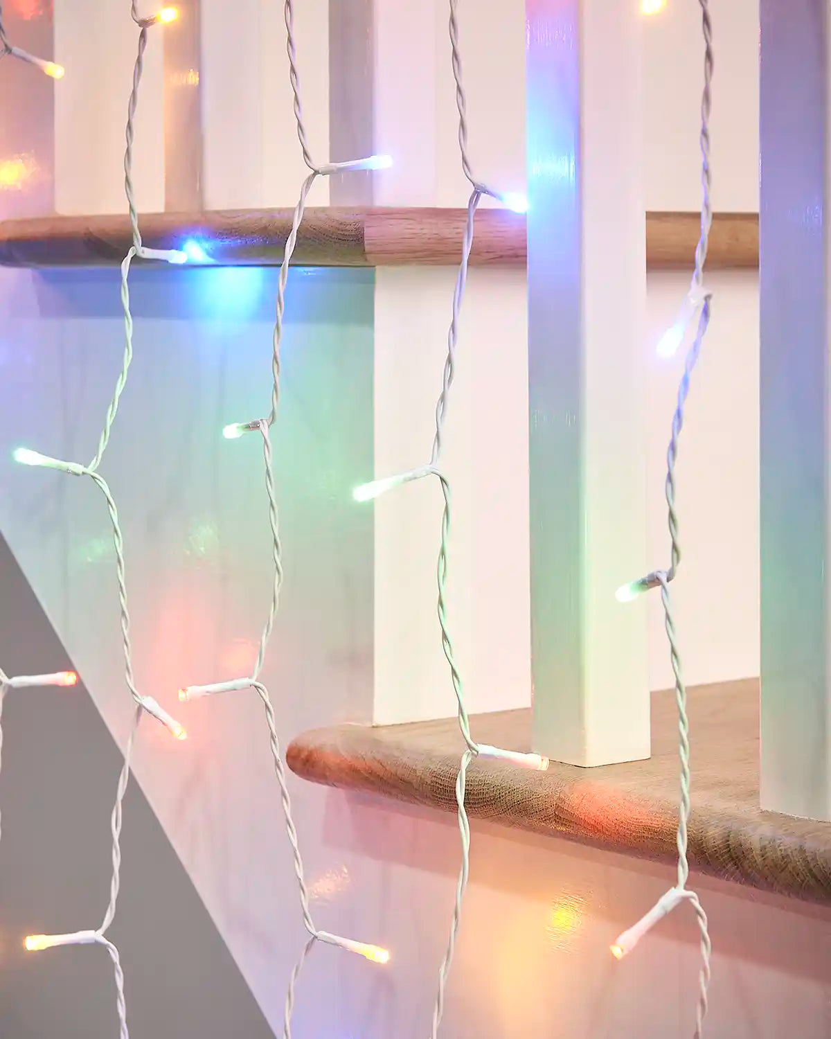Close-up of multi-colour curtain lights on white cable hanging near a wooden stair rail.