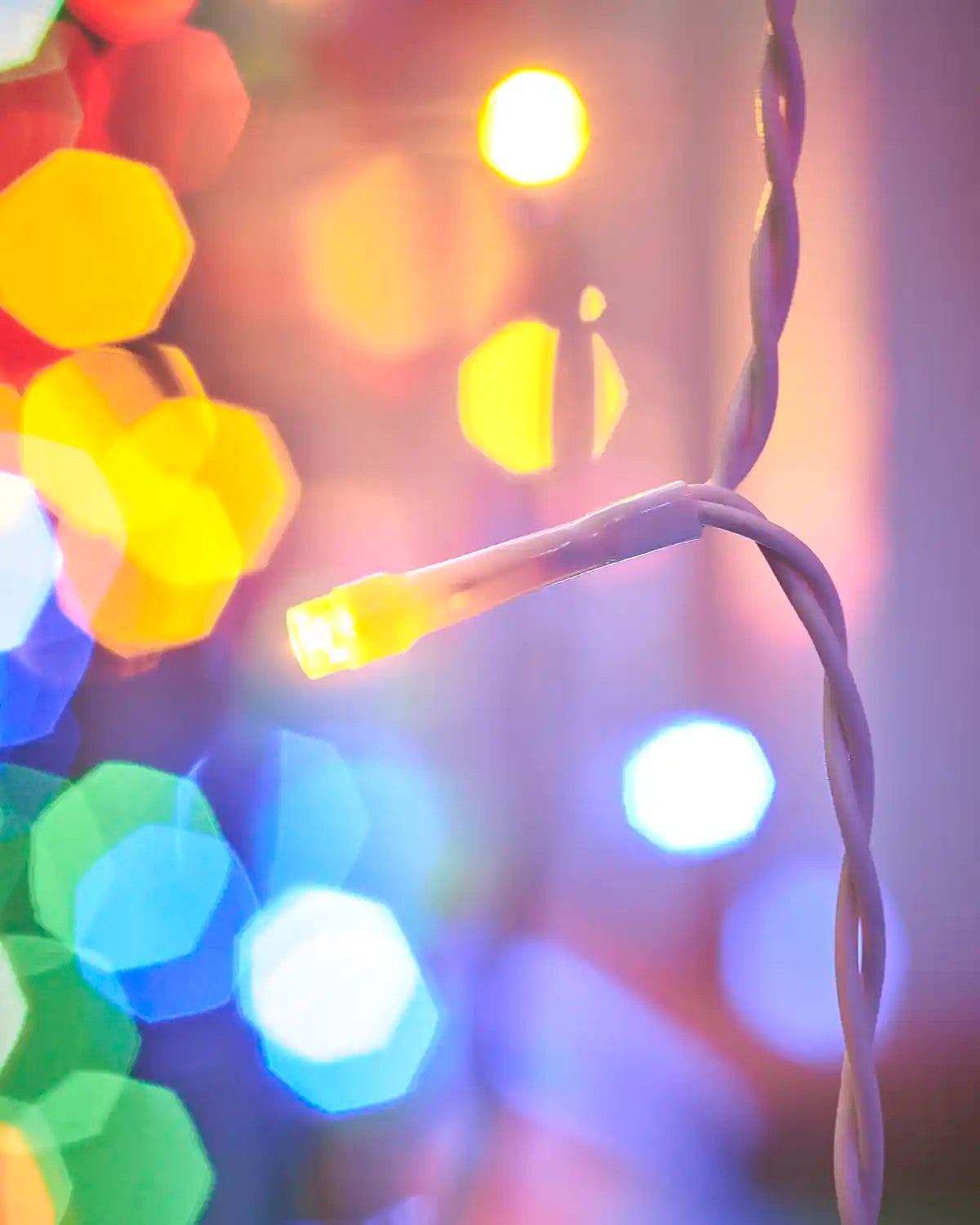 Close-up of a yellow LED on white cable with multi-colour lights in the background.