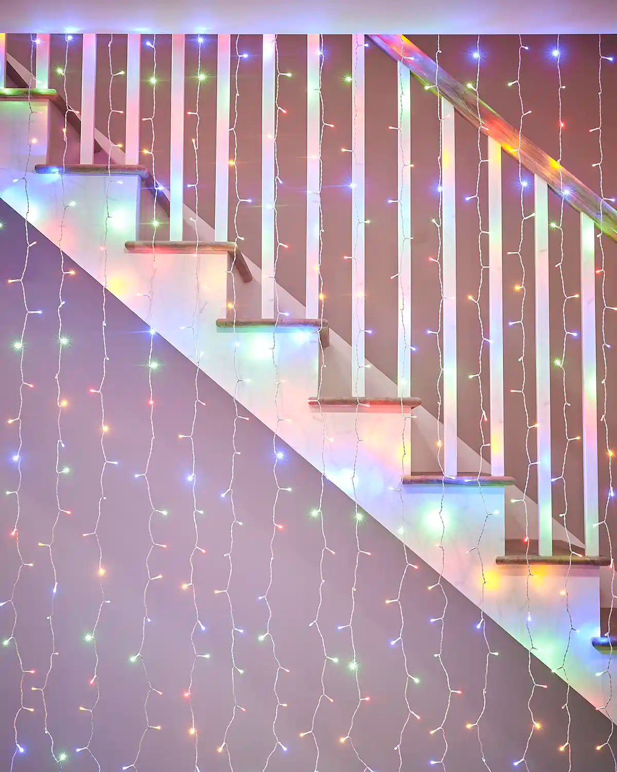 Multi-colour curtain lights on white cable displayed along a staircase bannister.
