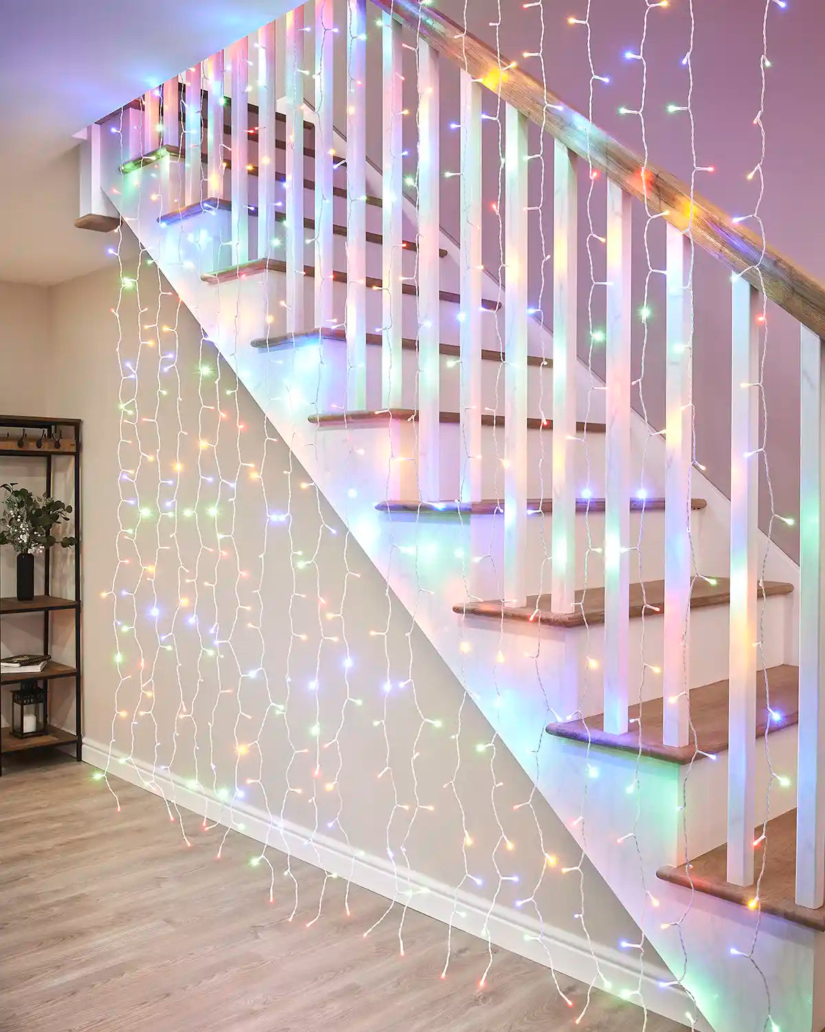 Multi-colour curtain lights on white cable hanging beside an indoor staircase.