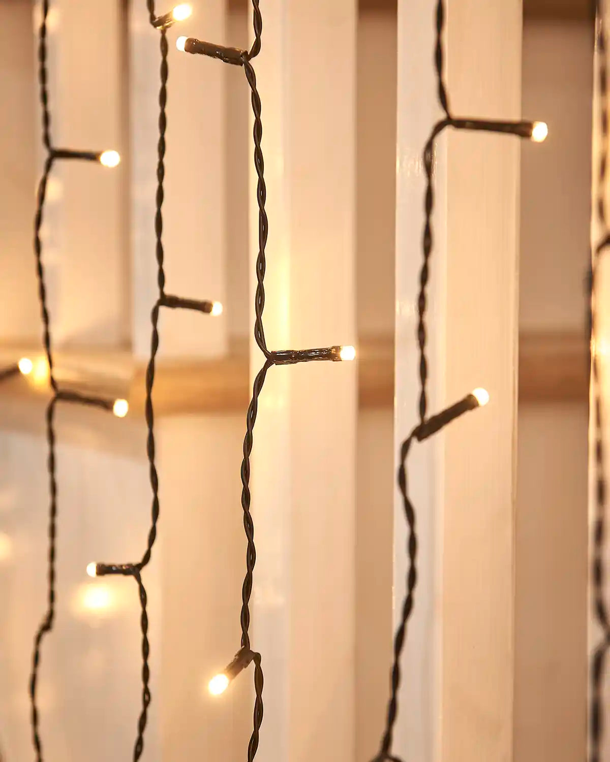Close-up of warm white curtain lights on black cable hanging near white stair spindles.