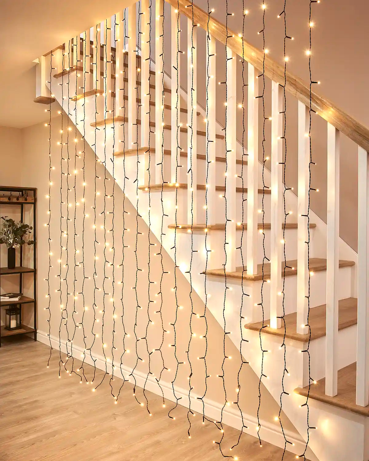 Warm white curtain lights on black cable hanging beside an indoor staircase.