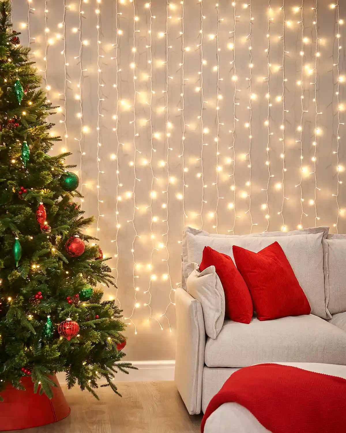 Warm white curtain lights on white cable displayed on a wall behind a sofa and Christmas tree.