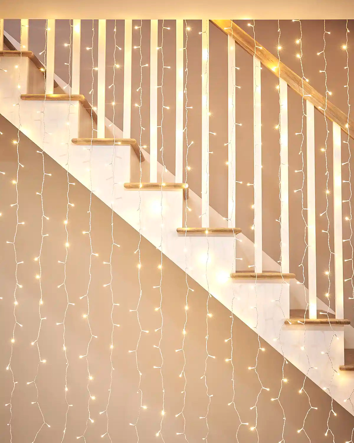 Warm white curtain lights on white cable displayed along a staircase bannister.