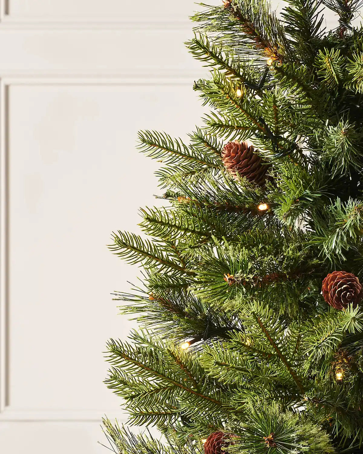 Close-up of 3.5 ft natural pine Christmas tree branches with pinecones and warm white lights