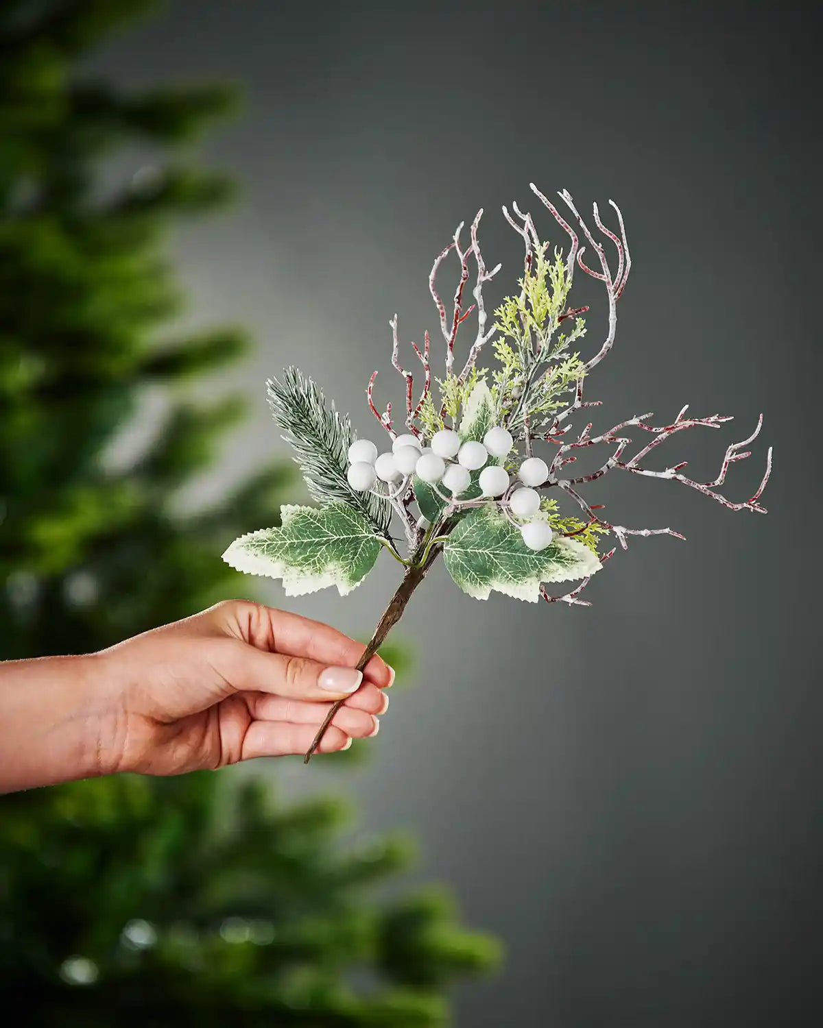 31 cm white artificial frosted berries pick held beside a Christmas tree
