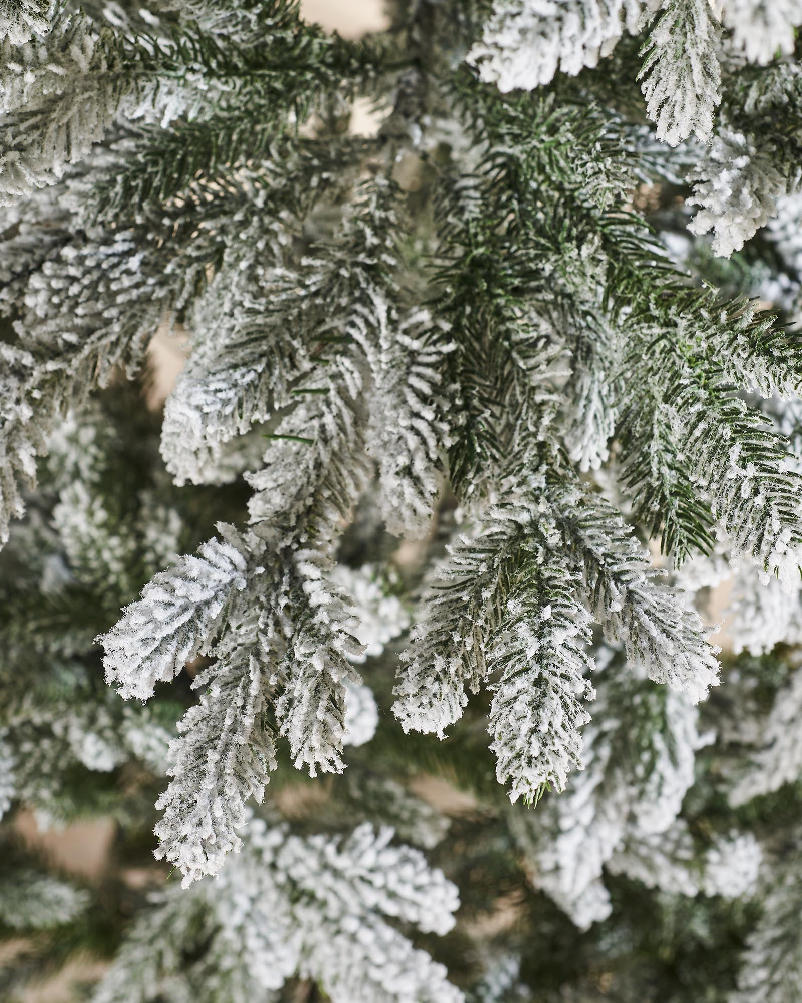 Luxury snow-flocked artificial Christmas tree with soft, snow-dusted tips and a full-bodied, naturalistic shape. Features hinged branches for easy assembly and storage, providing a reusable, elegant centerpiece that captures the charm of a rustic winter wonderland.