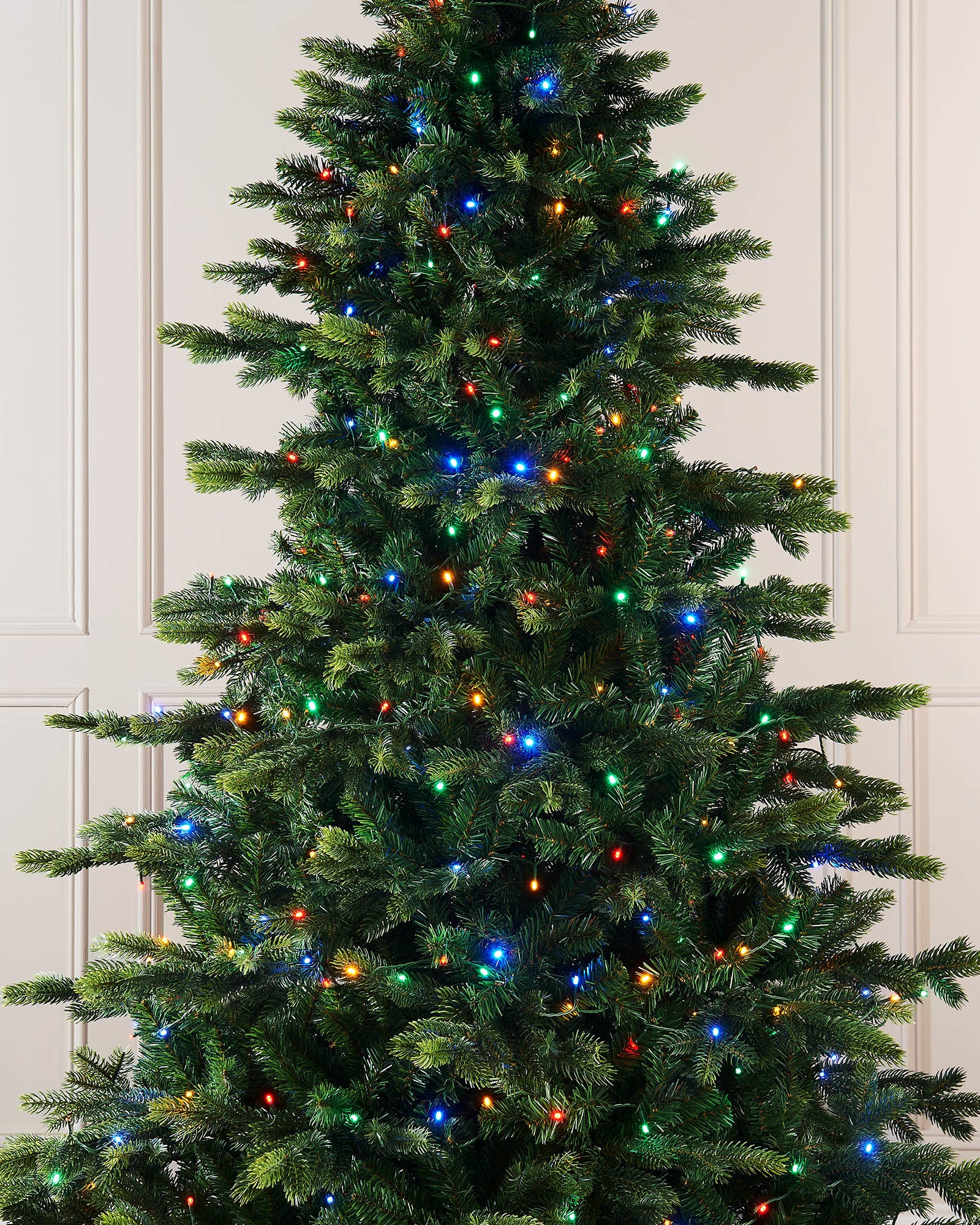 Decorated Christmas tree with colorful lights against a white paneled wall.