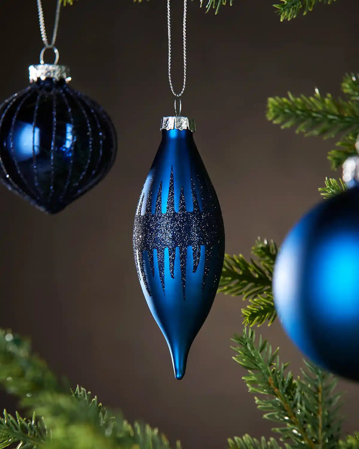 3 Blue glass Christmas baubles hanging on a tree branch with a brown background