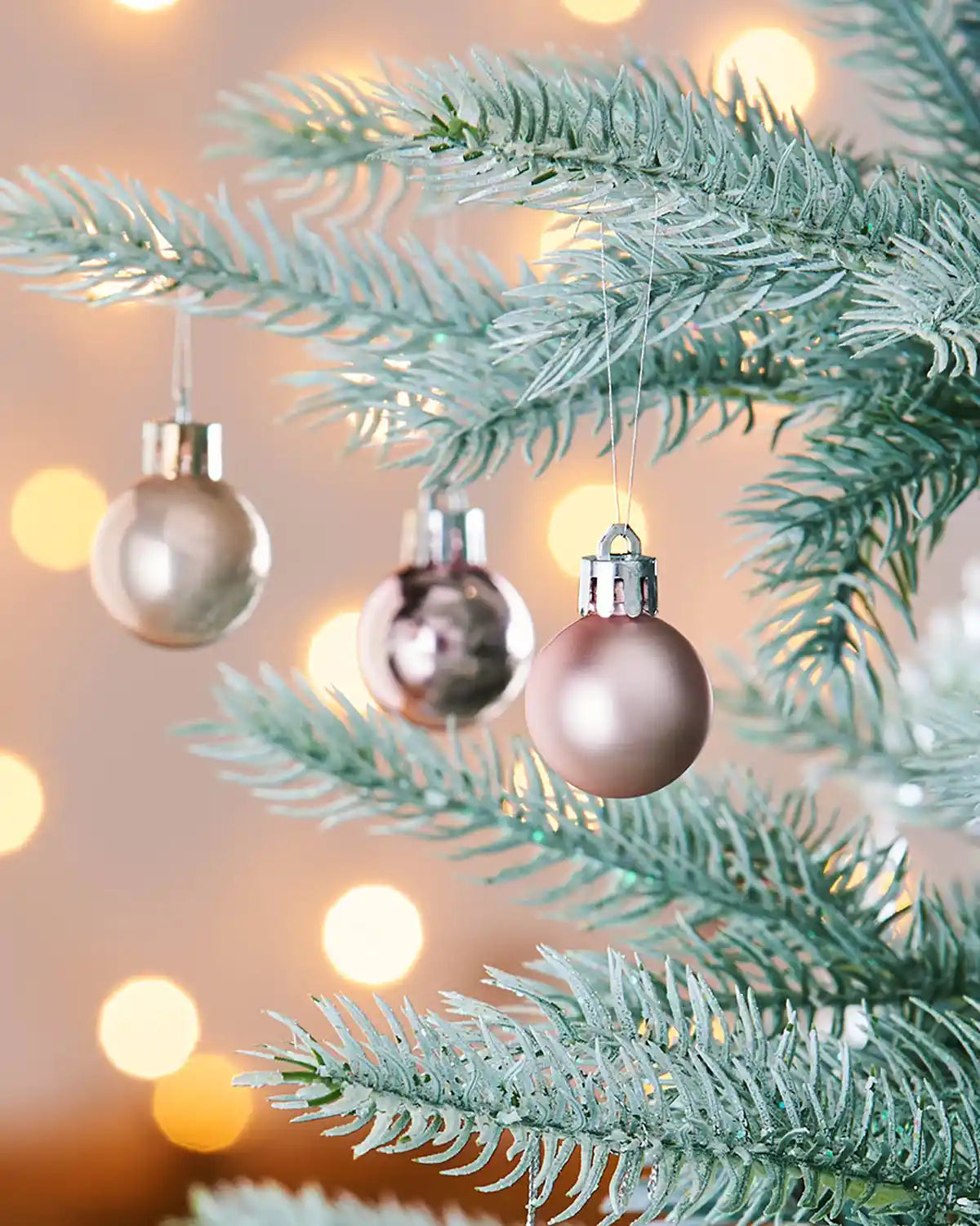 3 Decorative Pink Christmas baubles on a tree branch with a warm, blurred background