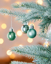 3 Green Christmas baubles hanging on a green tree branch with blurred lights in the background