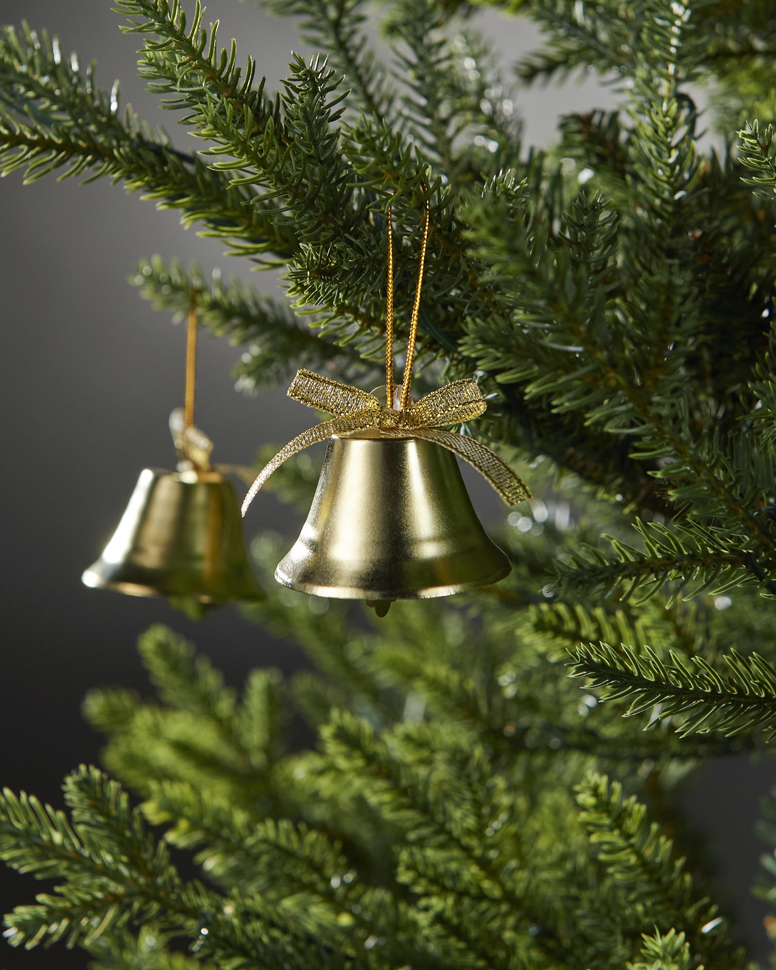 Gold bells with ribbons hanging on a Christmas tree against a dark background