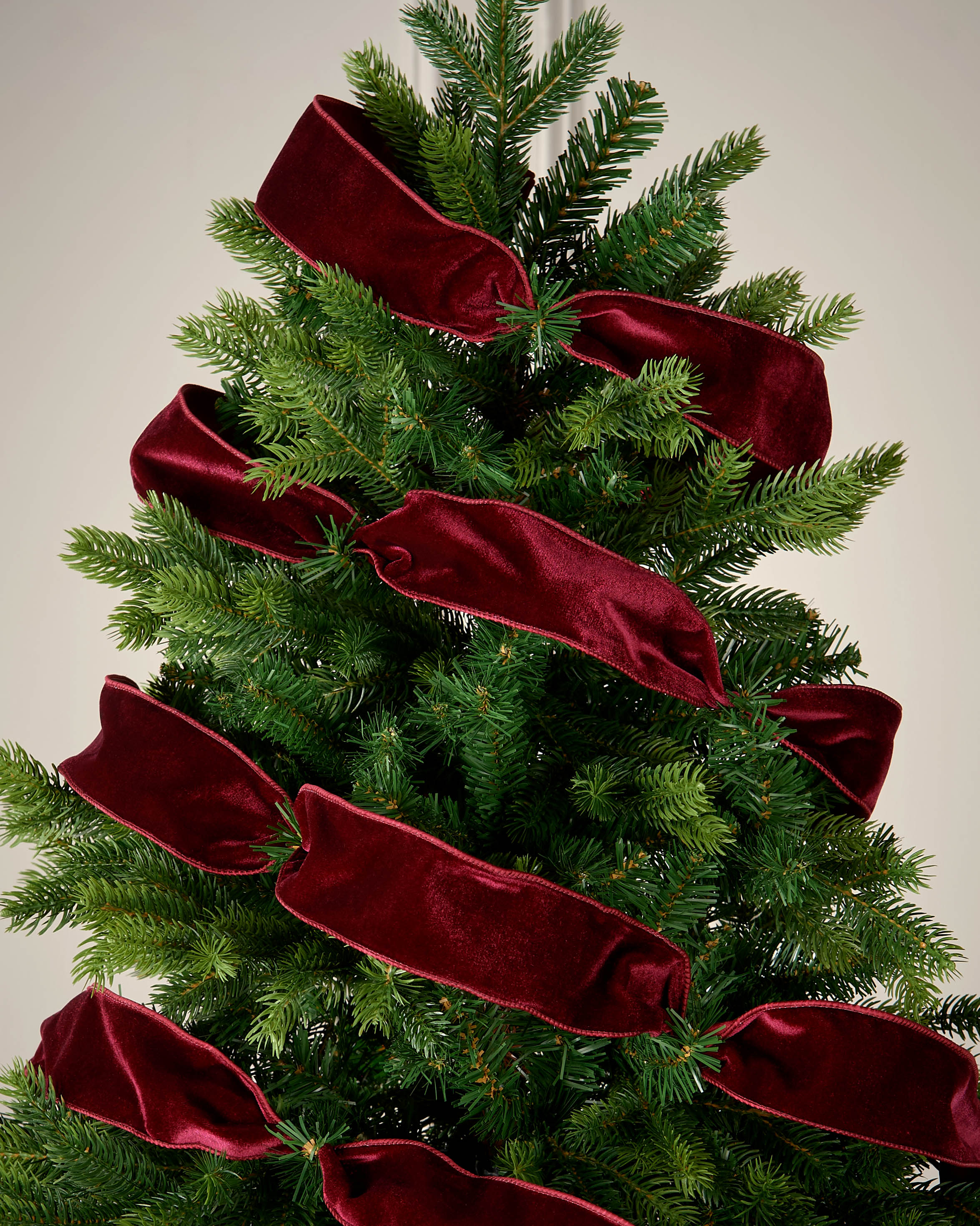 Decorative Christmas tree with red velvet ribbons on a plain background