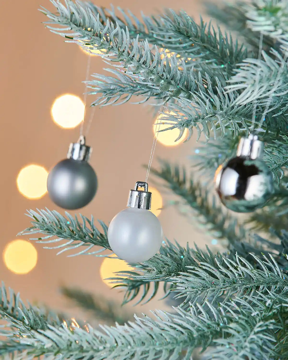3 silver baubles on a frosted tree with blurred lights in background