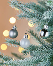 3 silver baubles on a frosted tree with blurred lights in background