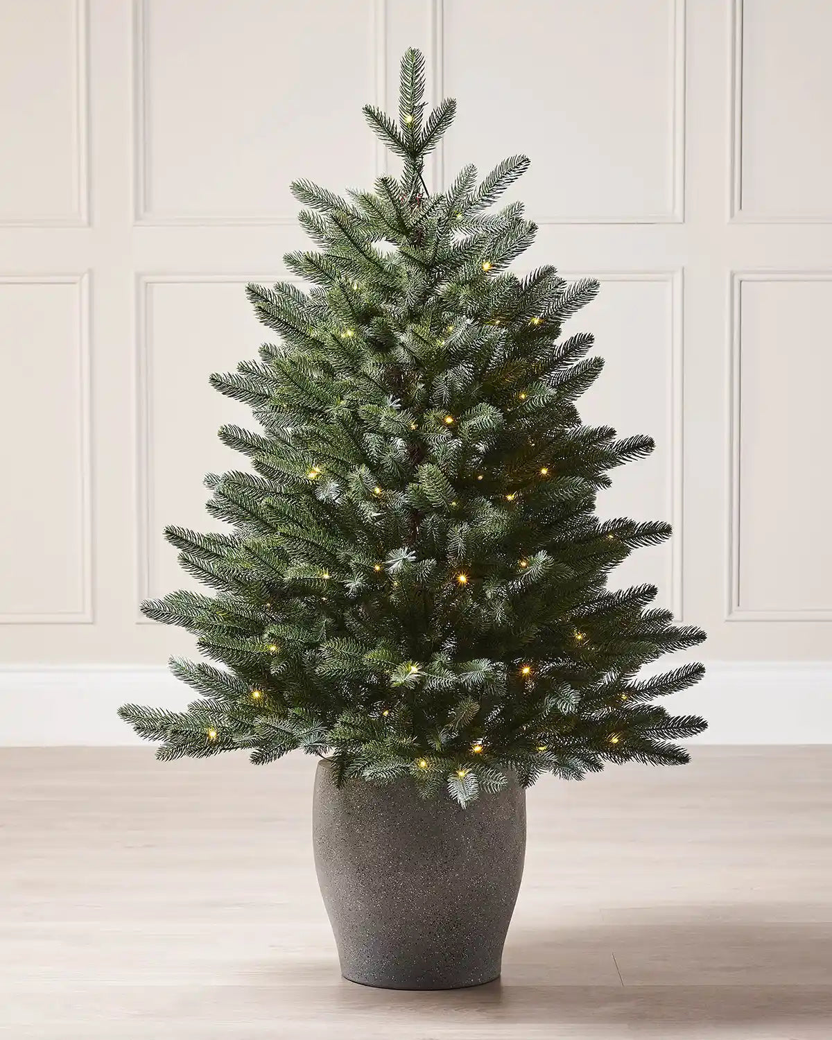 3ft Christmas tree with lights in a pot against a cream panel wall and wooden floor 