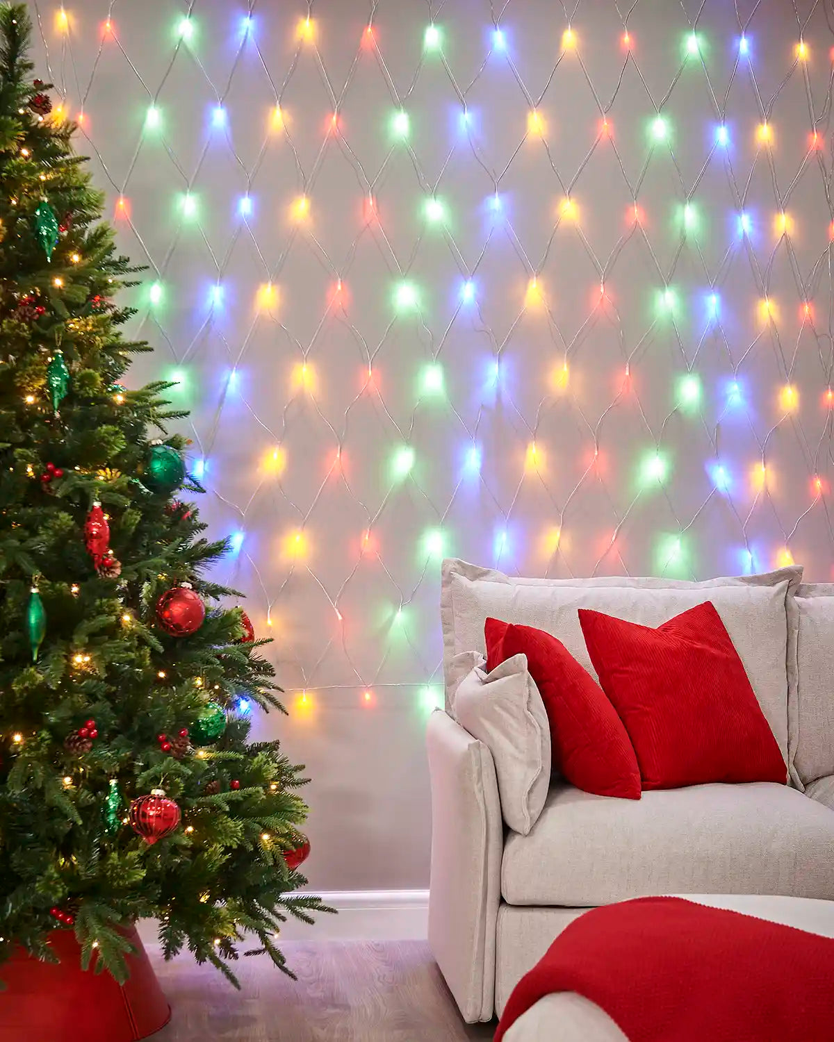 Multi-colour net lights displayed on a living room wall beside a Christmas tree and sofa.