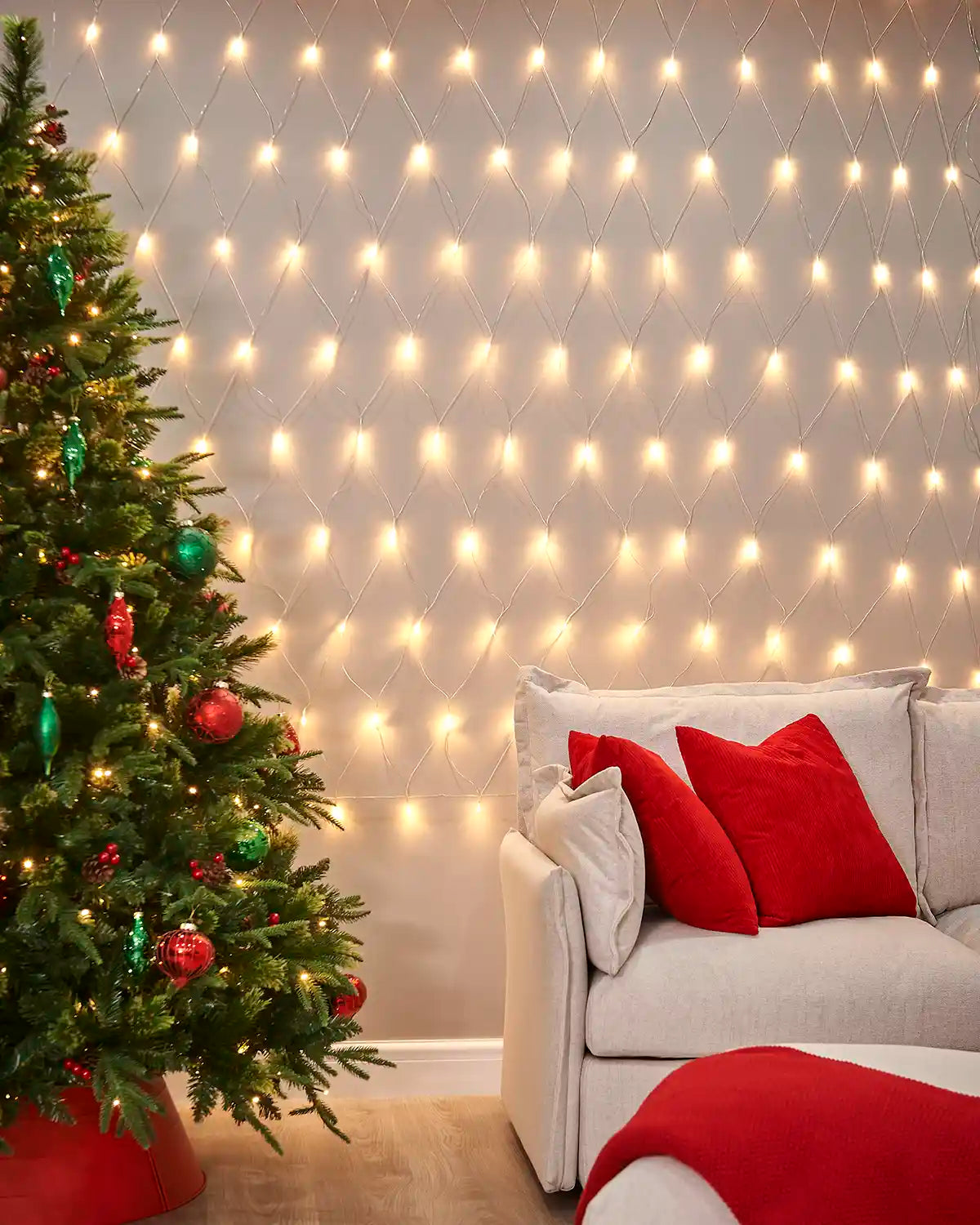 Warm white net lights displayed on a living room wall beside a Christmas tree and sofa.