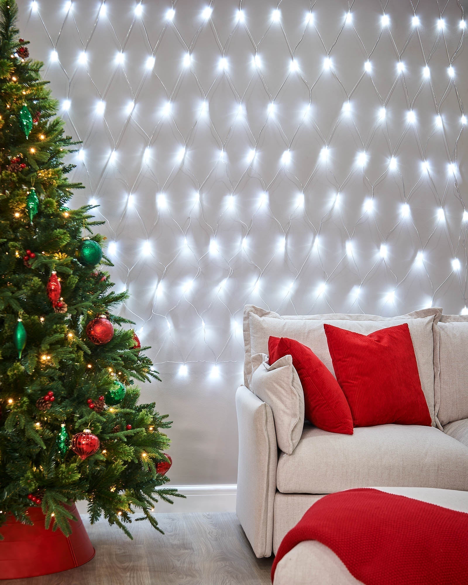 White net lights displayed on a living room wall beside a Christmas tree and sofa.