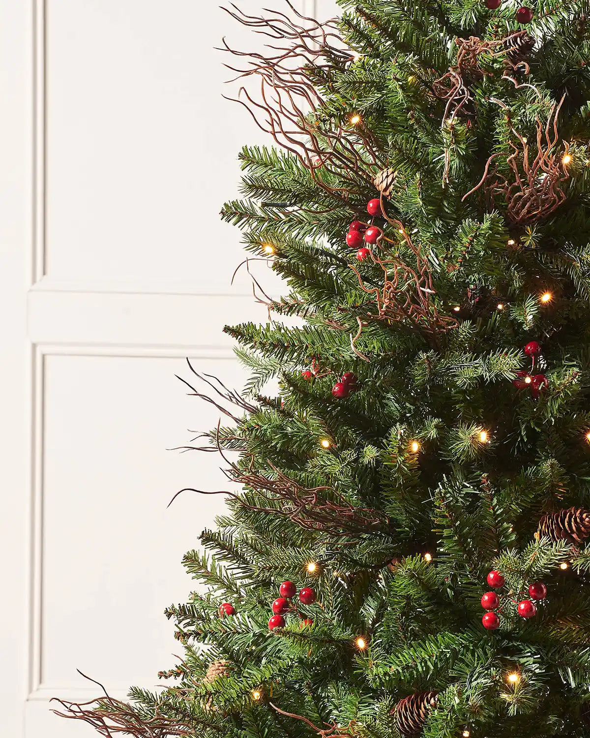 Close-up of pines and berries Christmas tree branches with red berries, twig accents and warm white lights