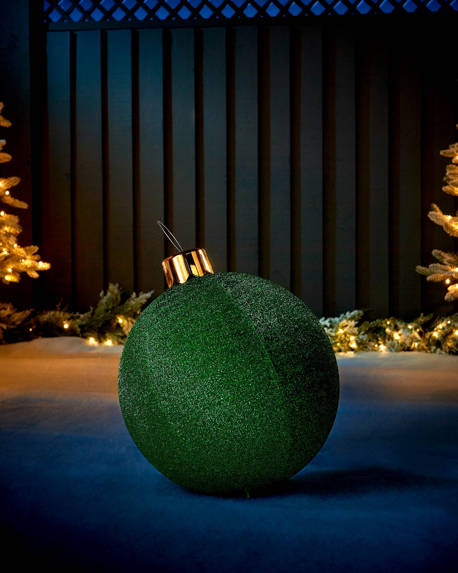 Green 45cm inflatable tinsel Christmas bauble with a gold cap in an outdoor festive display.