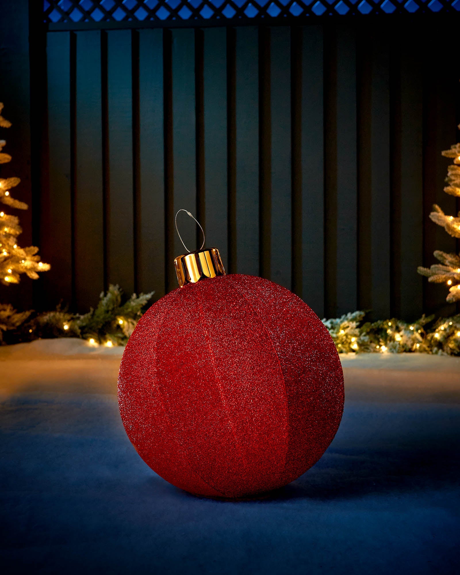 Red 45cm inflatable tinsel Christmas bauble with a gold cap in an outdoor festive display.