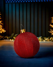 Red 45cm inflatable tinsel Christmas bauble with a gold cap in an outdoor festive display.