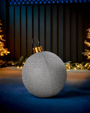 Silver 45cm inflatable tinsel Christmas bauble with a gold cap in an outdoor festive display.