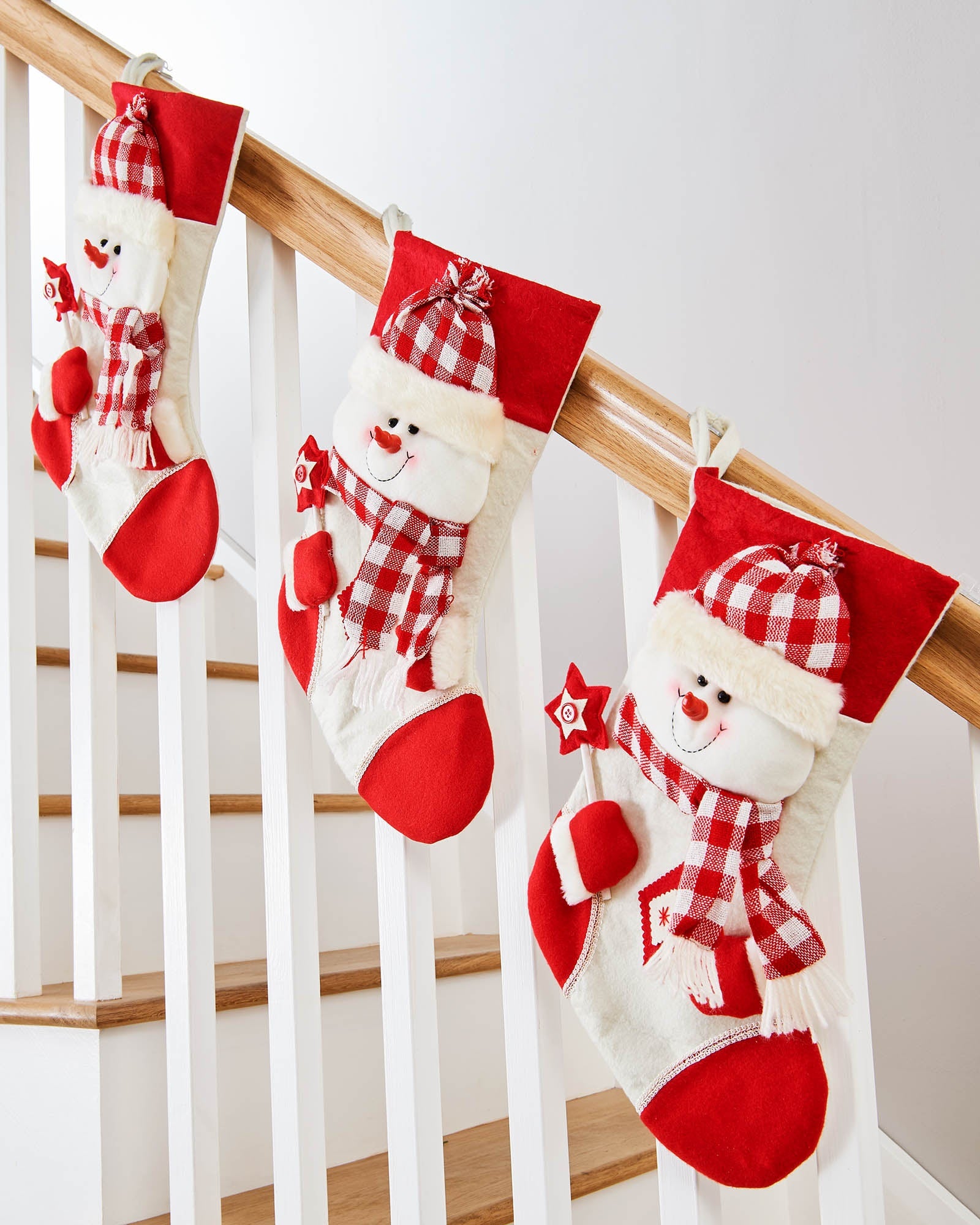 Three 48cm red and cream snowman Christmas stockings displayed on a stair rail