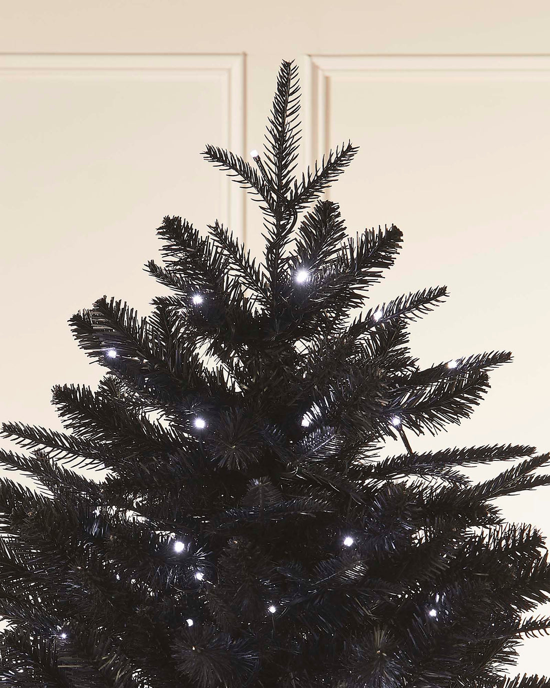 Close-up of a black Christmas tree with silver stars on a neutral background.