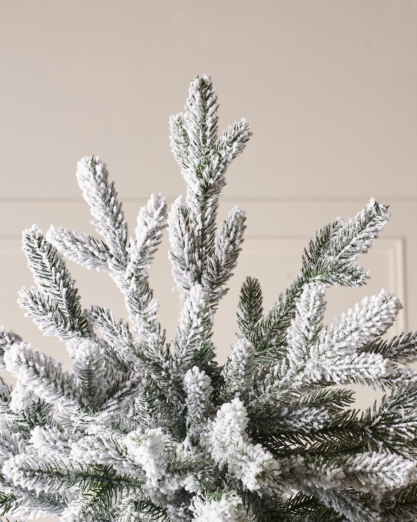 Luxury snow-flocked artificial Christmas tree with soft, snow-dusted tips and a full-bodied, naturalistic shape. Features hinged branches for easy assembly and storage, providing a reusable, elegant centerpiece that captures the charm of a rustic winter wonderland.