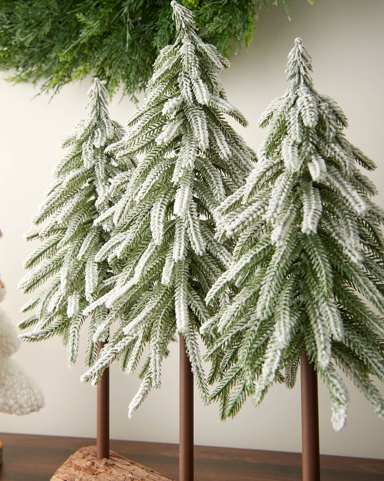 Decorative Christmas trees with snow on a wooden stand against a neutral background