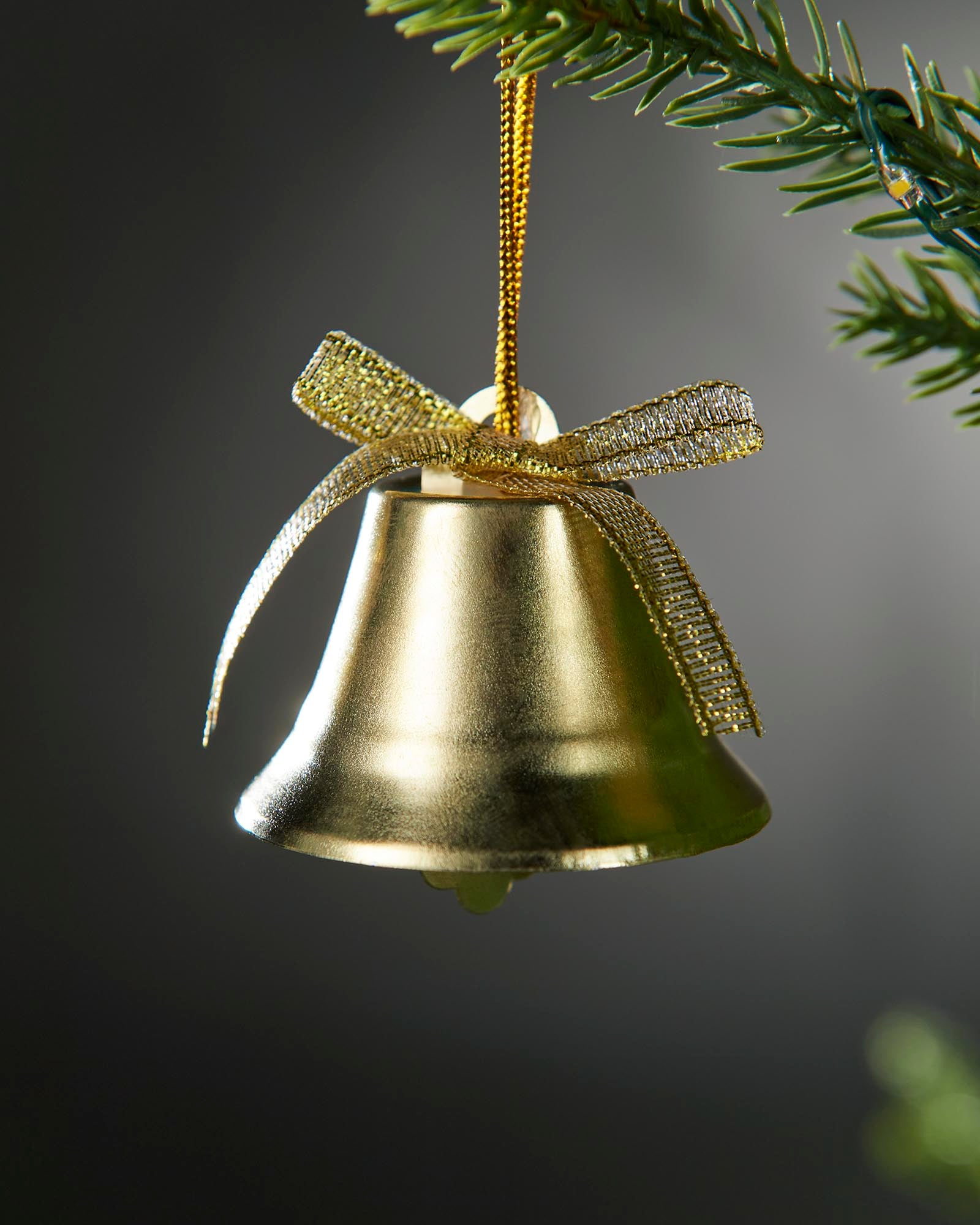Gold bell ornament with a gold ribbon on a dark background