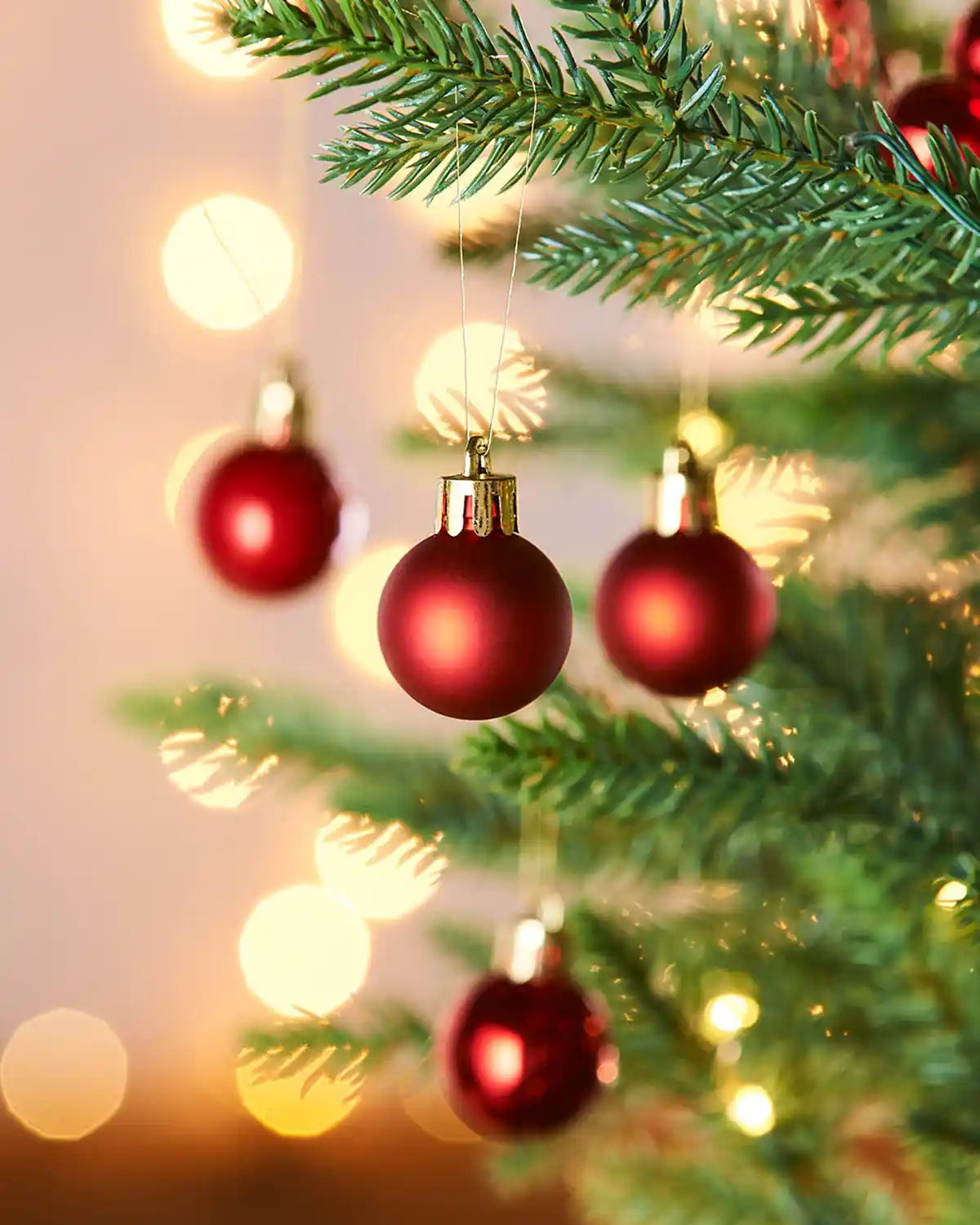 4 Red Christmas baubles on a tree with blurred lights in the background