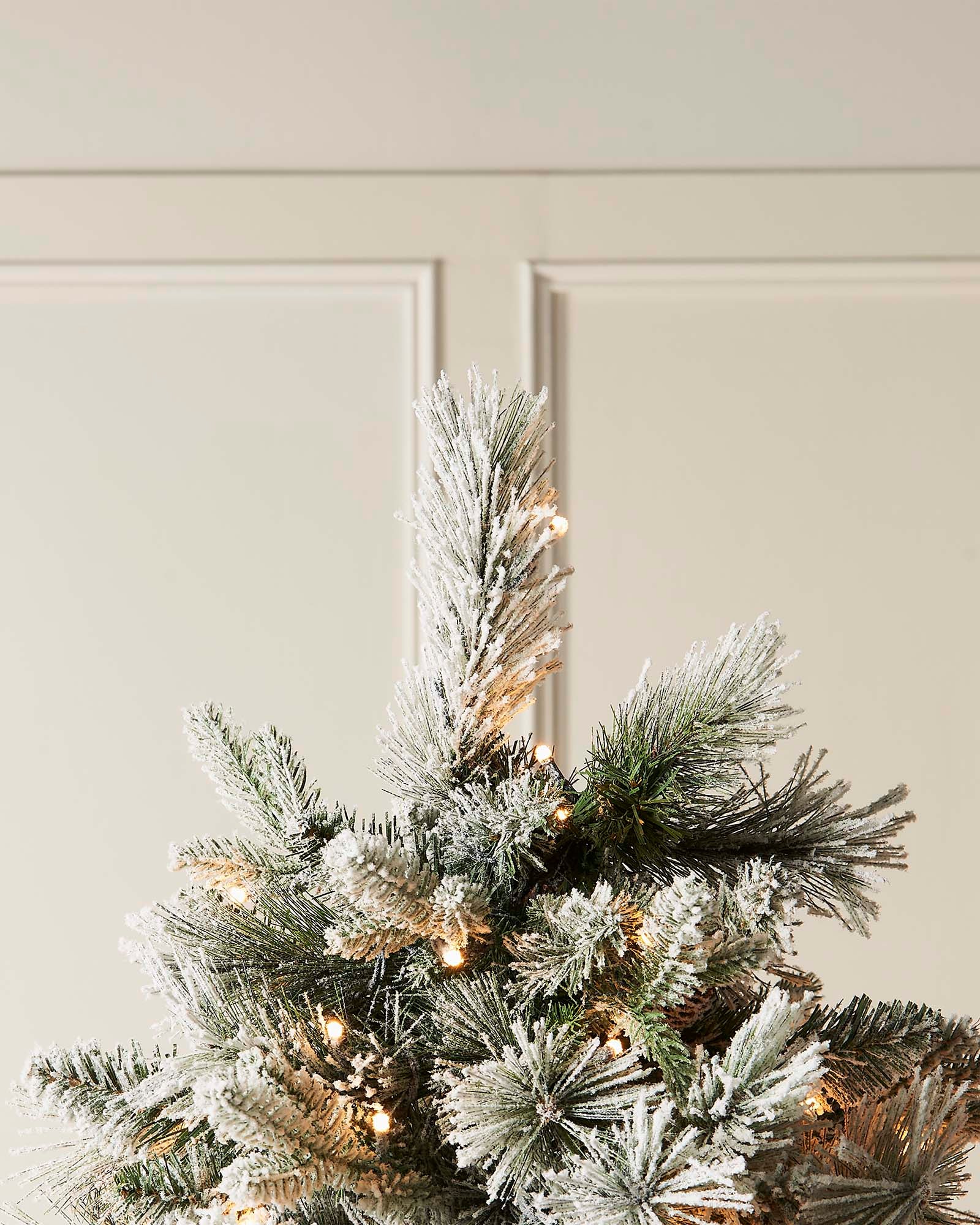 Frosted Christmas tree with gold accents against a neutral background.