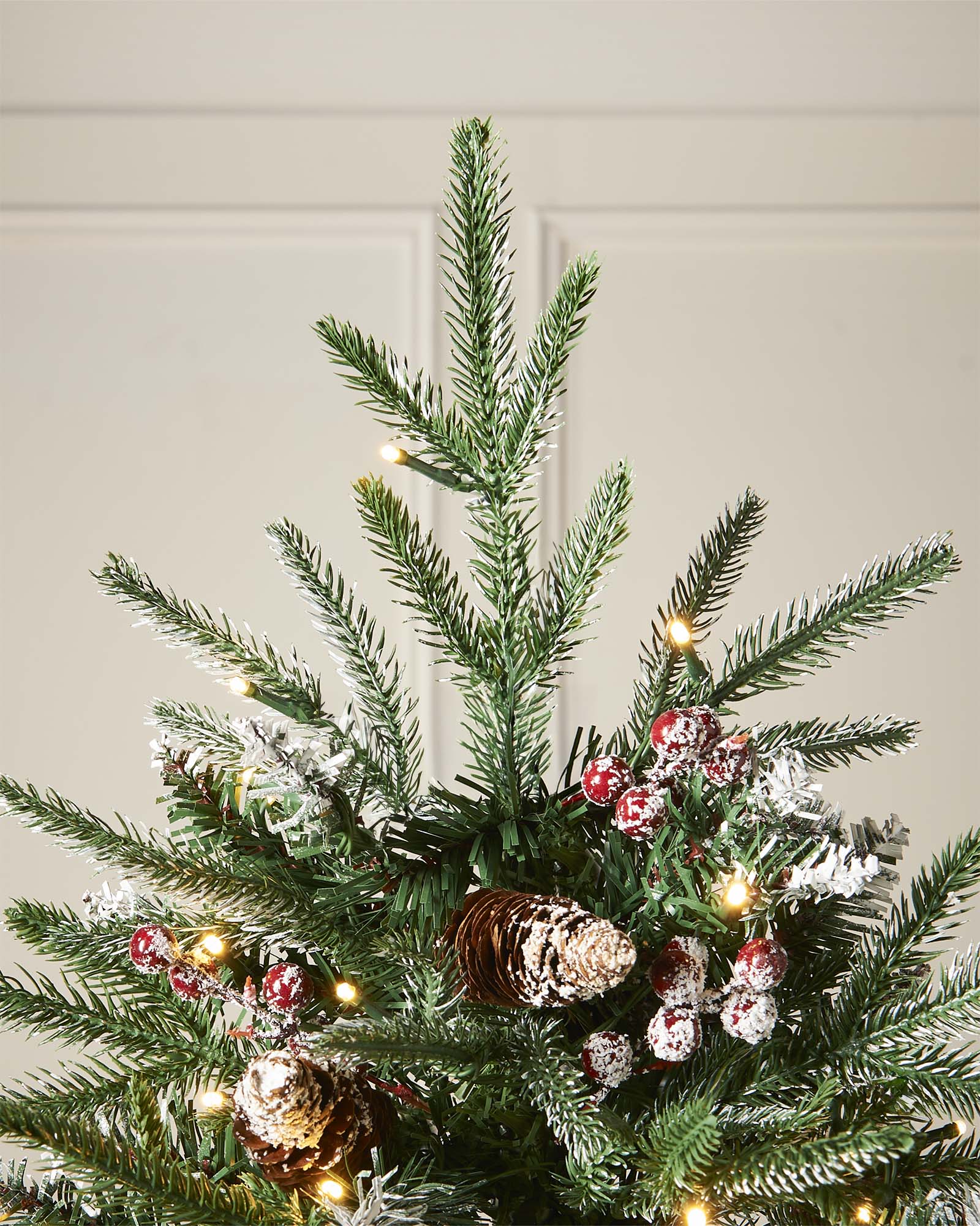 Pre-lit frosted Norwegian Spruce Christmas tree with snow-dusted branches, natural pinecones, and red berries. Features warm white multi-function LED lights and a lifelike PE and PVC tip construction.