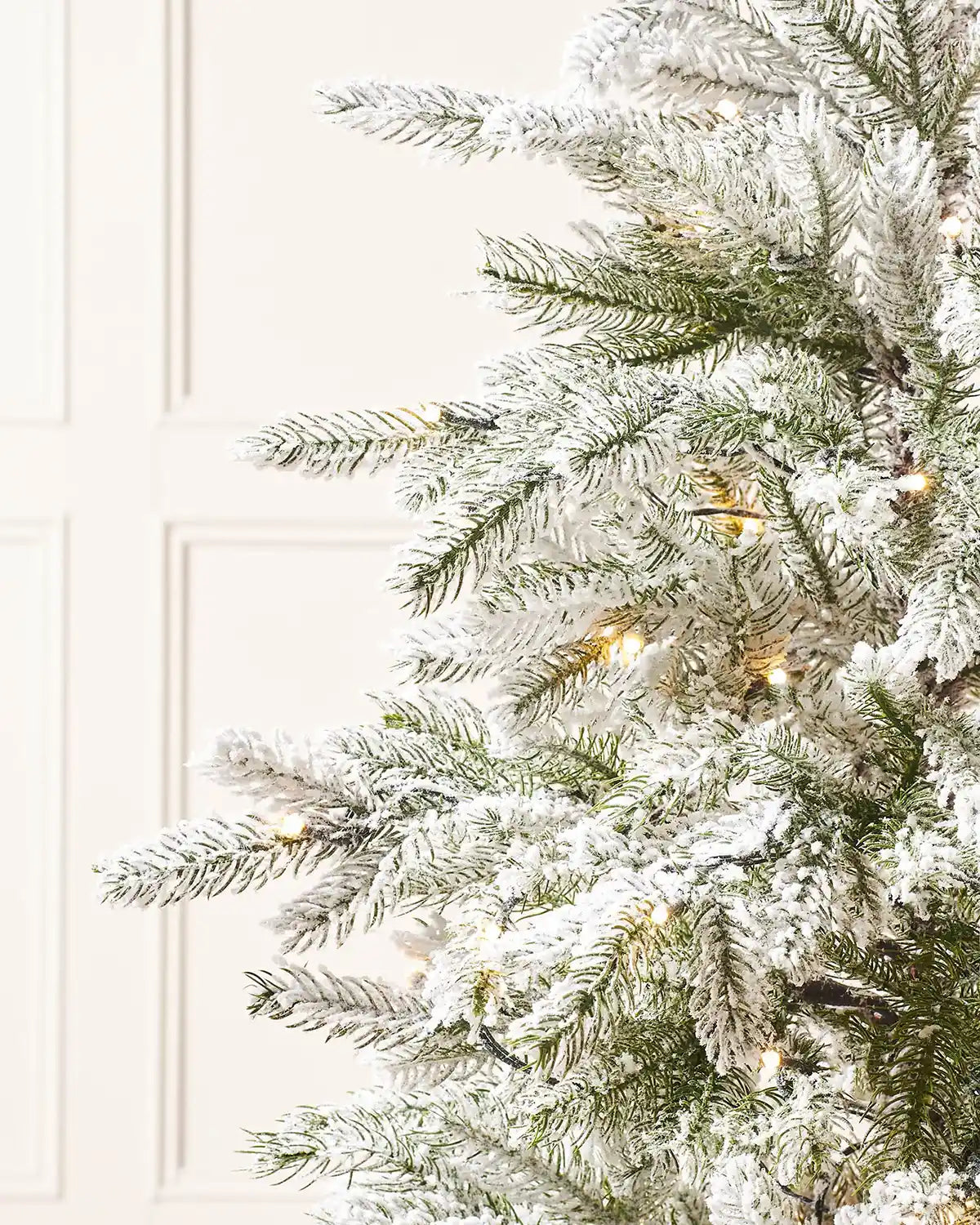 Close-up of snow flocked Christmas tree branches with warm lights and realistic mixed foliage