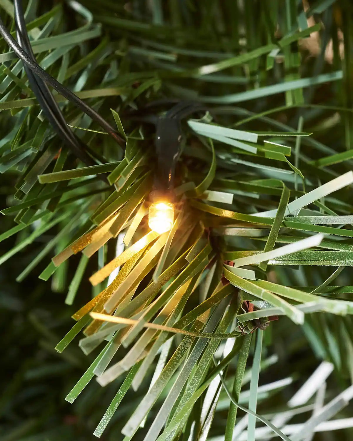 Close-up of a warm white LED nestled among frosted artificial Christmas tree branches