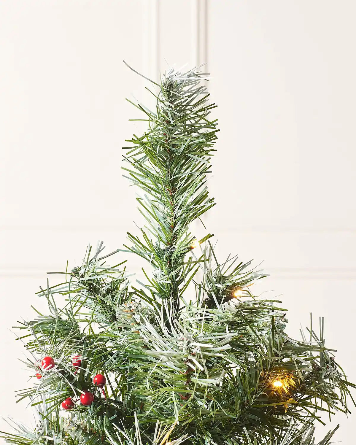Close-up of the frosted tree top with red berries and warm white lights