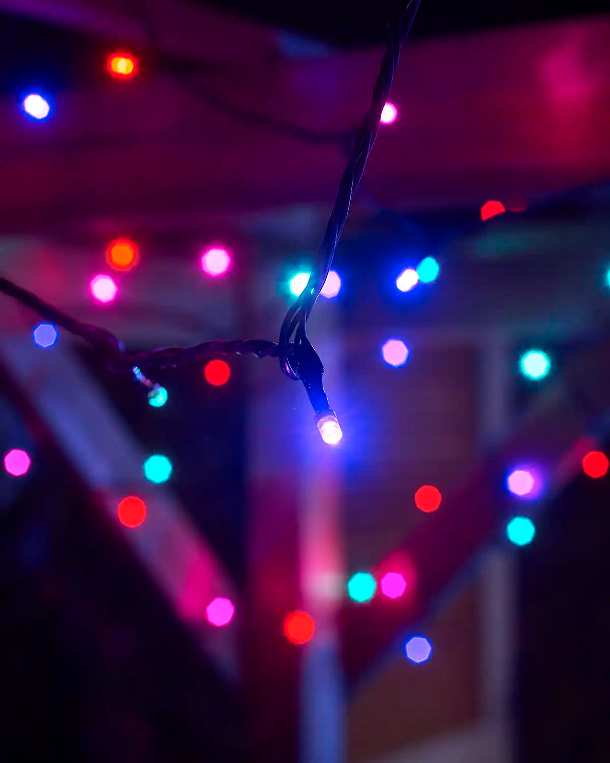 Close-up of colourful Aurora LEDs on black cable hanging beneath a wooden structure.