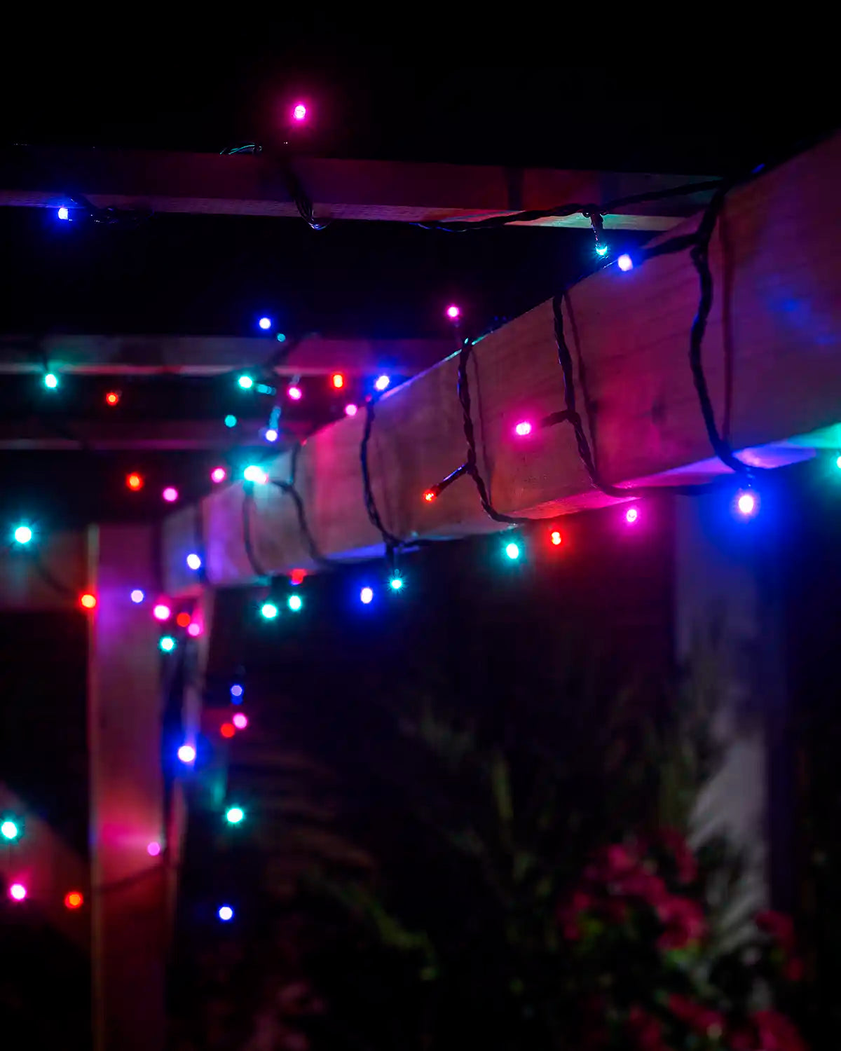 Aurora string lights with black cable wrapped around a wooden pergola at night.