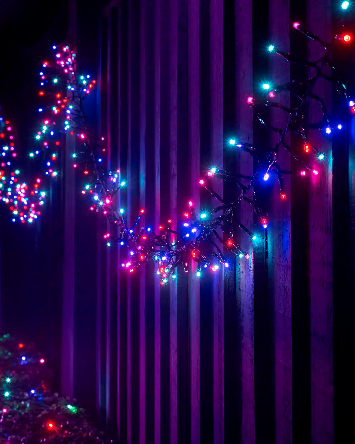 Aurora cluster lights on black cable arranged along a wooden fence at night.