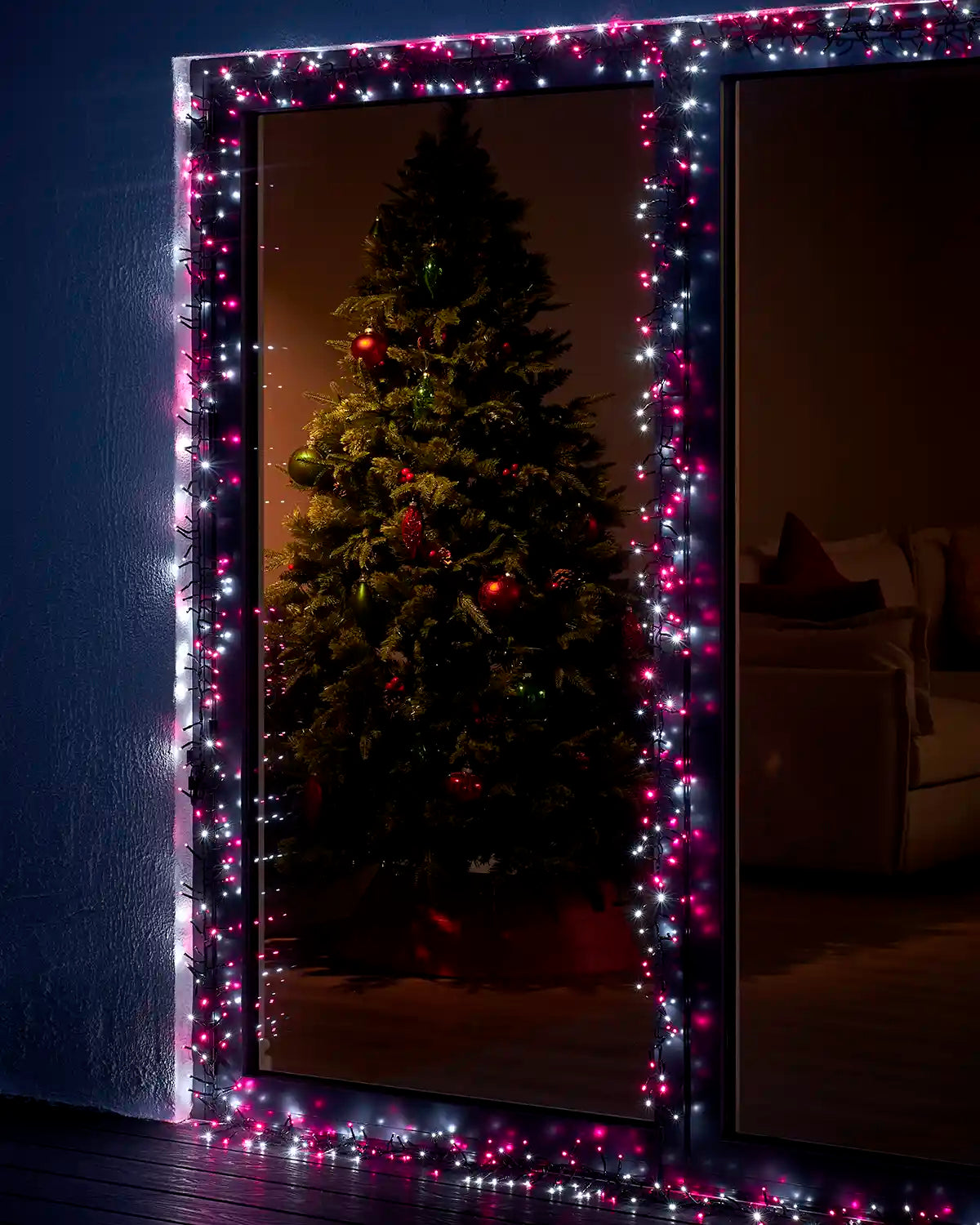 Pink and white cluster lights framing a glass door with a Christmas tree visible indoors.