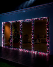 Pink and white cluster lights displayed around large outdoor window frames at night.