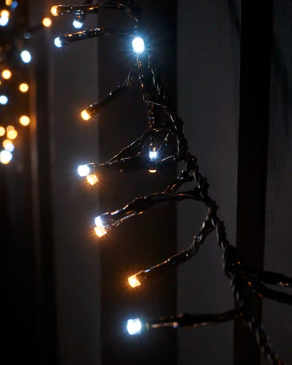 Detail view of warm white and white LEDs on black cable wrapped around a fence post.