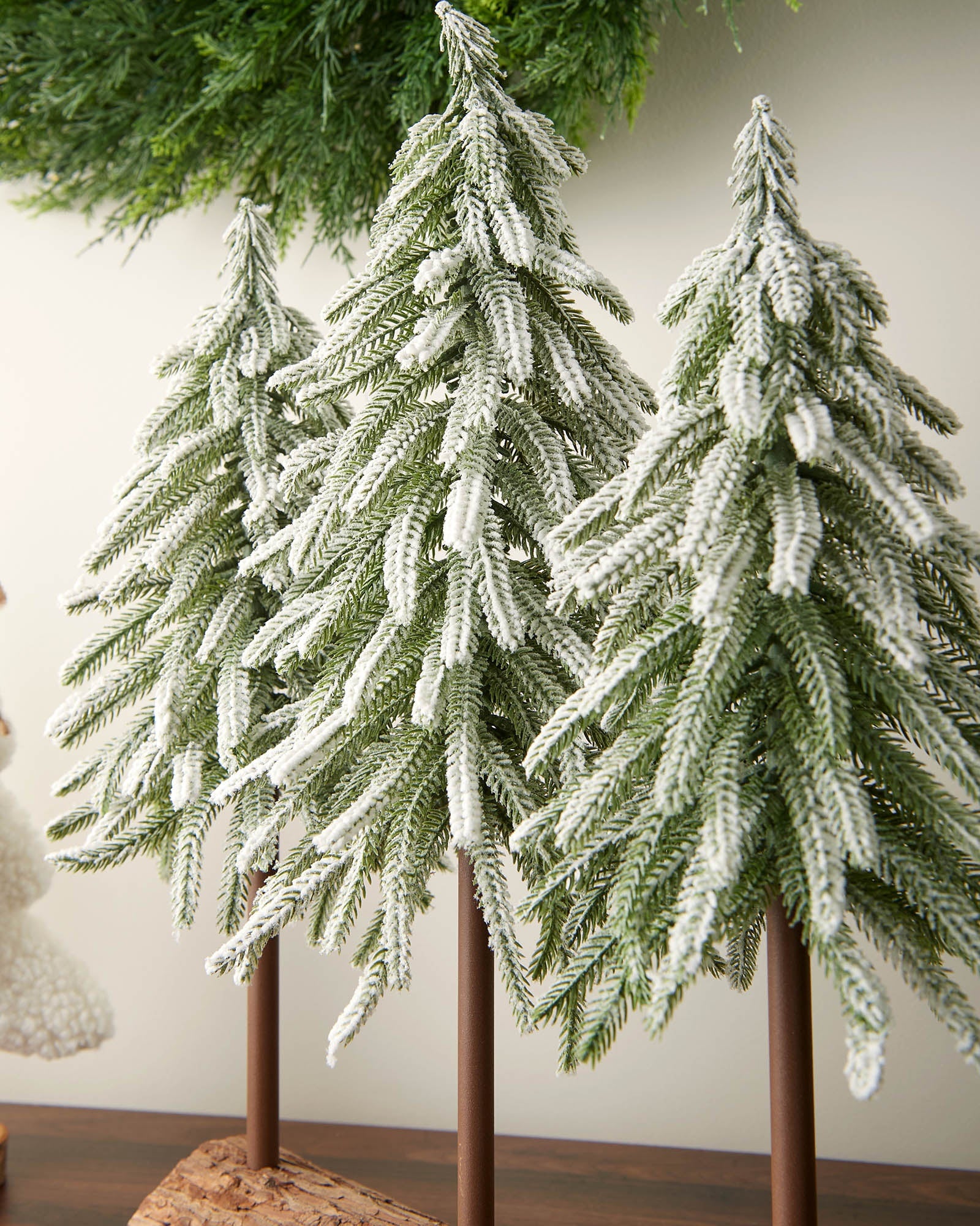 Detail view of three snow-flocked fir trees arranged on a log base.