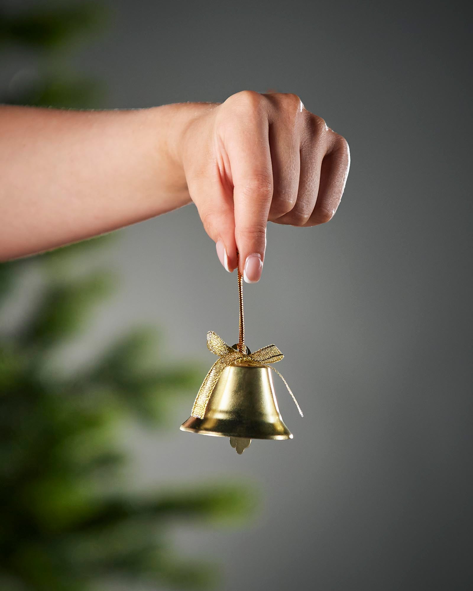 Hand holding a small gold bell against a gray background