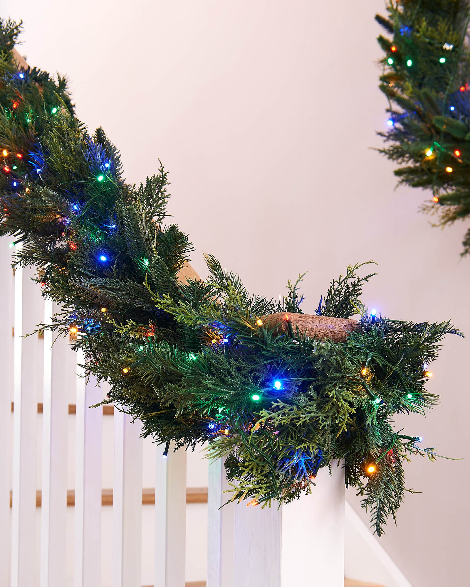 Decorative Christmas wreath with lights on a white railing.