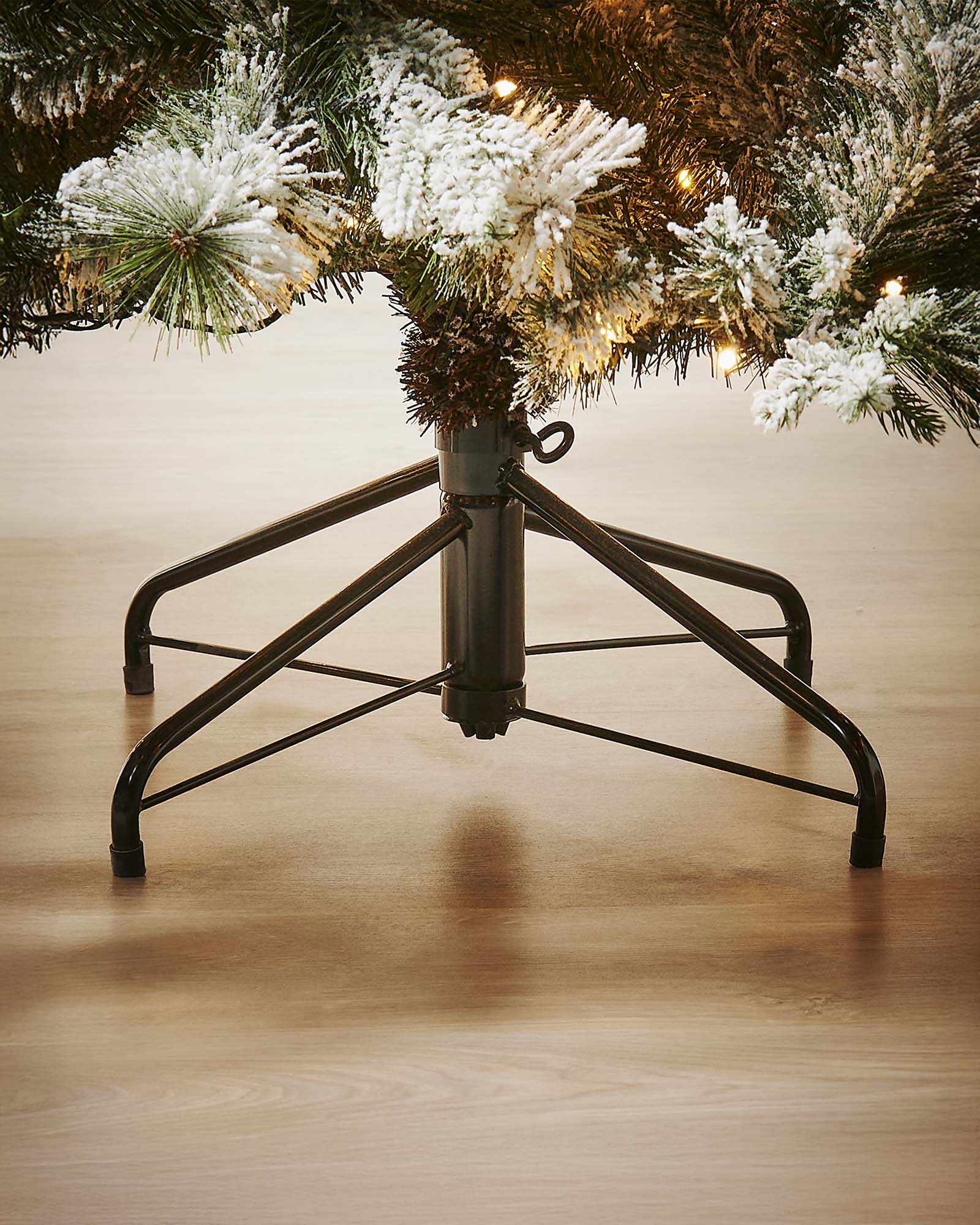Black metal Christmas tree stand with a decorated tree on a wooden floor.
